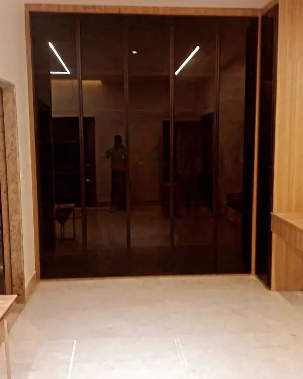 A glimpse into a spacious walk-in wardrobe featuring floor-to-ceiling doors made of dark, reflective glass. This design creates a sense of depth and luxury, with integrated lighting that adds a dramatic effect to the bedroom.