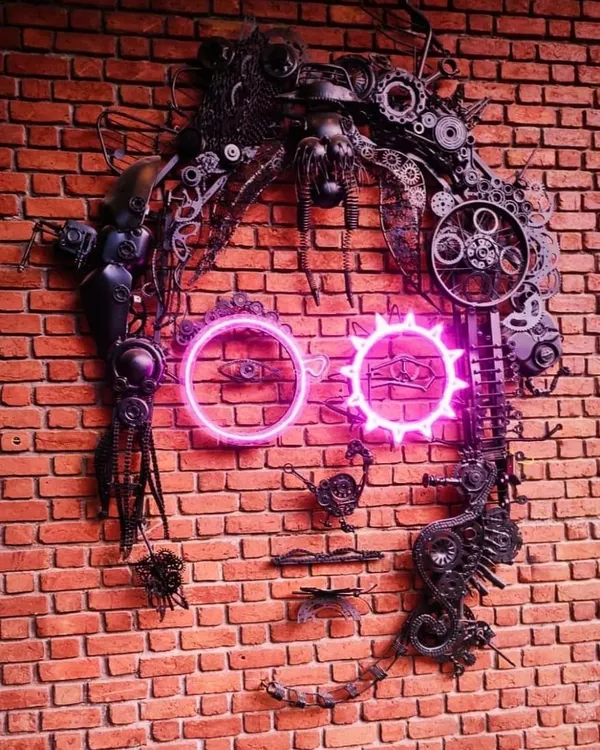 A different view of our John Lennon junk art portrait. Every piece of scrap, from chains to cogs, was carefully selected and welded to build the texture and form of his face, with neon glasses adding a modern twist.
