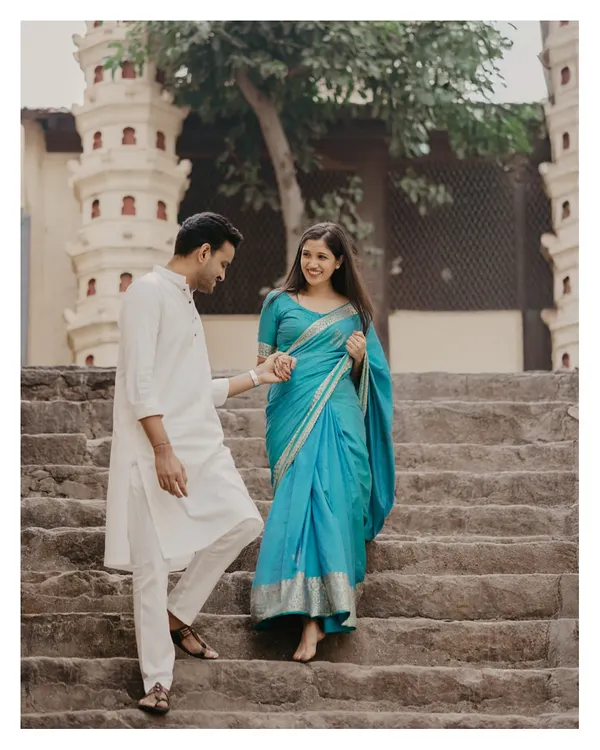 A candid moment of the couple descending the historic stone steps at Banganga, showcasing the beautiful drape of the turquoise saree.