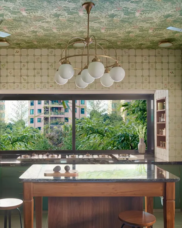 This kitchen, with its view of the lush outdoors, is the heart of the home, designed for slow mornings and shared meals. The island becomes a natural gathering spot, while the large window invites nature in, creating a space that feels both expansive and intimate.