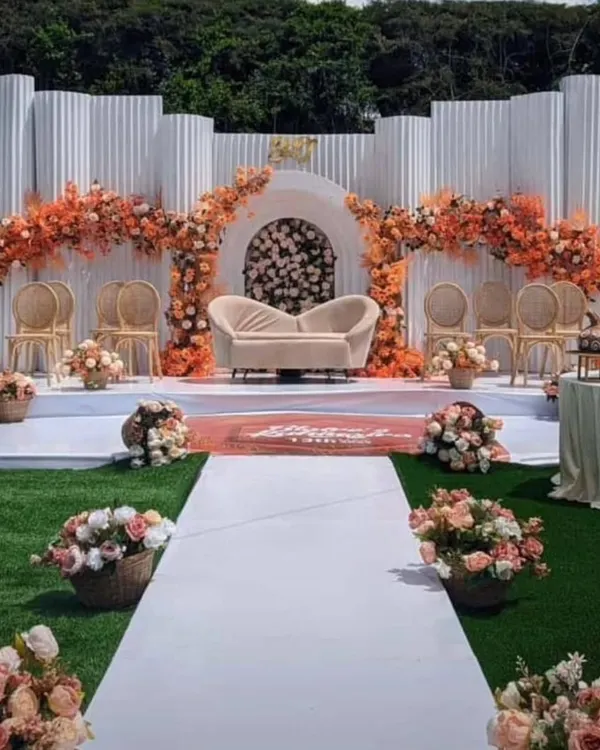 This stunning outdoor stage was designed for a daytime engagement, featuring a modern white corrugated backdrop and lush arches of orange and peach florals. I create these large scale, bespoke setups to make a grand statement at any venue.
