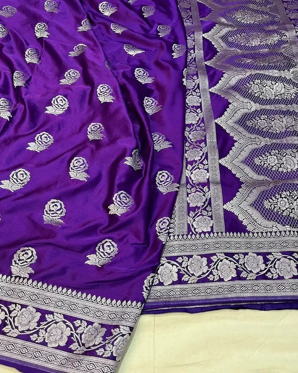 This royal purple Banarasi Mashru silk saree features an intricately woven silver border and delicate rose butis all over. The pallu has a traditional heavy design, making it a statement piece.