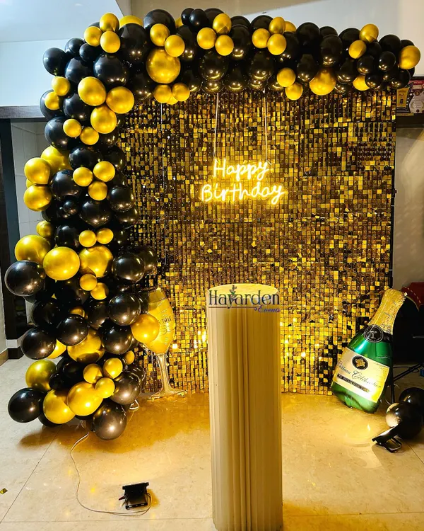 A classic black and gold theme, perfect for a sophisticated party. This setup features a gold sequin backdrop, a 'Happy Birthday' neon sign, and a full balloon arch. The champagne bottle balloon adds a fun, celebratory touch.