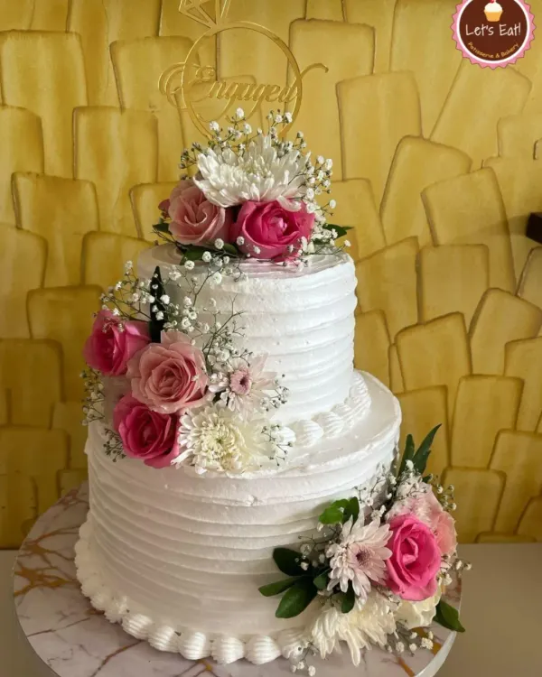 A classic two-tiered engagement cake with white ridged buttercream. I decorated it with a cascade of fresh pink and white roses and baby's breath for a touch of natural beauty and romance.