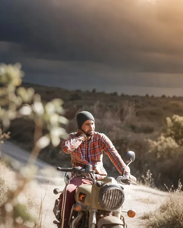 An old-school, rugged portrait of a man on his motorcycle. The dramatic, cloudy sky and earthy tones give this photo a cinematic and adventurous feel.