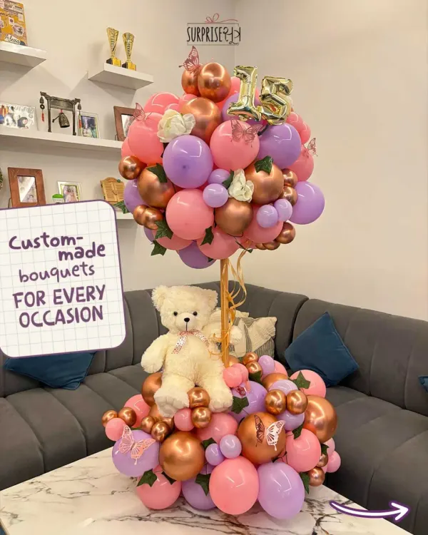 I create custom-made bouquets for every occasion. This one features a sweet teddy bear nestled in a two-tiered arrangement of pink, purple, and rose gold balloons, perfect for a 15th birthday.
