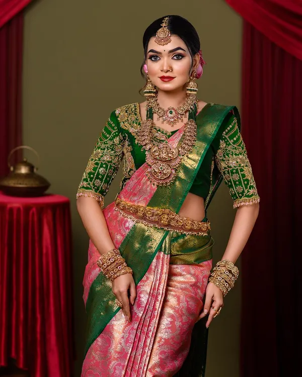 A full-length view of a stunning South Indian bride. We styled her in a beautiful pink and green Kanjeevaram saree with perfectly draped fabric and heavy temple jewellery.
