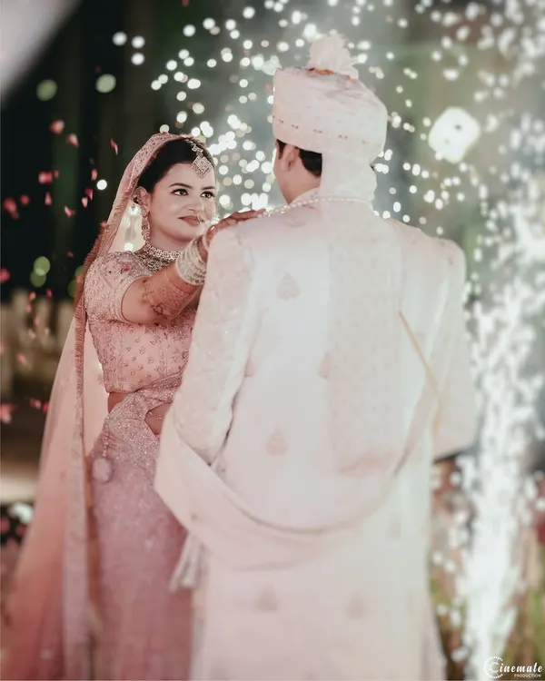 The Varmala ceremony, captured from behind the groom, focusing on the bride's expression as she places the garland. The sparklers add a touch of magic to this pivotal moment.