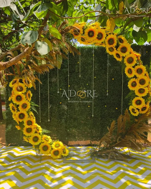 A 'Sunflower Aura' selfie booth. This circular arch made of bright sunflowers against a green hedge wall provides a cheerful and vibrant spot for guests to take photos.