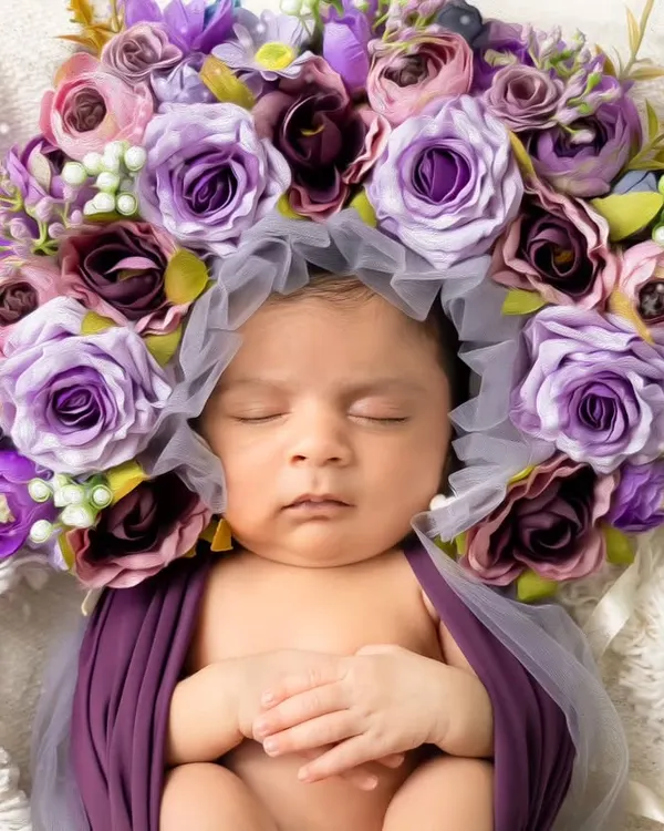 A peaceful newborn rests, swaddled in purple and crowned with a halo of flowers. This is the essence of our newborn artistry sessions.