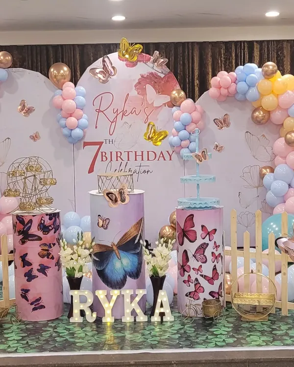 The main stage for a 7th birthday with a butterfly theme. This setup uses pastel pink and blue balloons, butterfly-printed pedestals, and light-up letters for the birthday girl's name.
