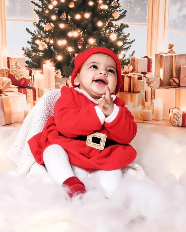 A joyful baby dressed as Santa, clapping with delight in our winter wonderland studio setup. These sessions are perfect for holiday cards.