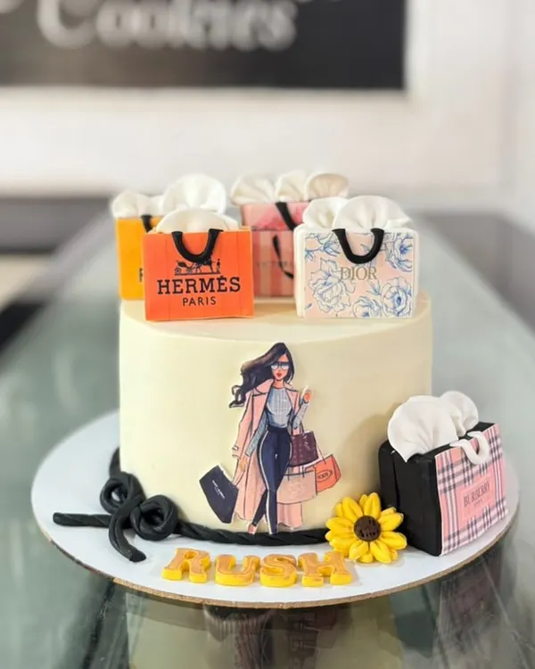 A fashion lover's dream cake, decorated with edible shopping bags from luxury brands like Hermes and Dior. It's a chic and stylish centerpiece for a birthday.