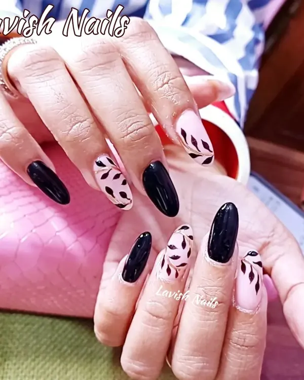 A chic and sophisticated design on almond-shaped nails, featuring a mix of solid black and accent nails with hand-painted black leaves on a sheer pink base.