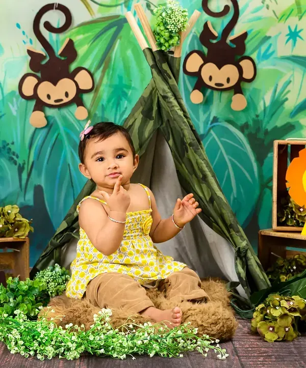 A baby girl sits in a jungle-themed setup, looking curious and sweet among her animal friends.