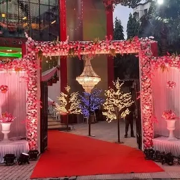 A grand entrance for a wedding at Grand Celebration banquet in Seawoods. The arch is covered in pink flowers, and the walkway is lined with illuminated trees, creating a warm and inviting welcome.