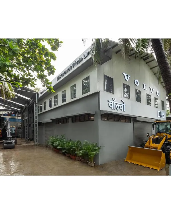 The finished exterior of the Volvo industrial facility, showing the two-story office block adjacent to the workshop space. The design provides a clean, modern corporate identity while being surrounded by greenery.