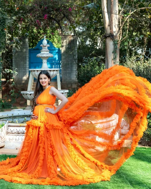 A stunning portrait of a mom-to-be in our vibrant orange ruffled gown, with the fabric creating a beautiful flying effect. This was taken in a garden with a classic fountain, adding a touch of elegance.