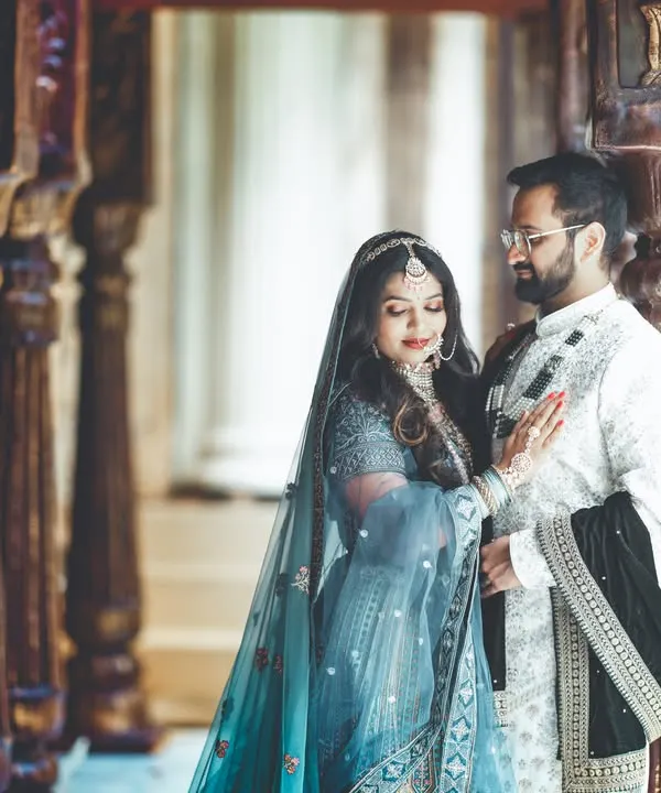 A quiet, intimate moment between a couple in beautiful traditional attire. The soft lighting and the historic-looking corridor create a timeless, romantic feel.