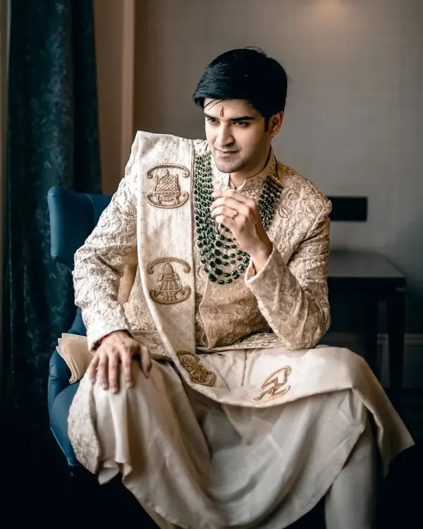 A classic, regal portrait of the groom seated, looking poised and ready for his wedding. The lighting highlights the rich texture of his traditional sherwani.