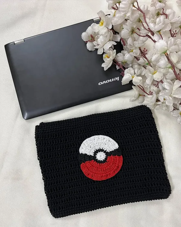 A handmade crochet laptop sleeve with a Pokémon theme, shown here next to a laptop for scale. It's a fun and protective way to carry your tech.
