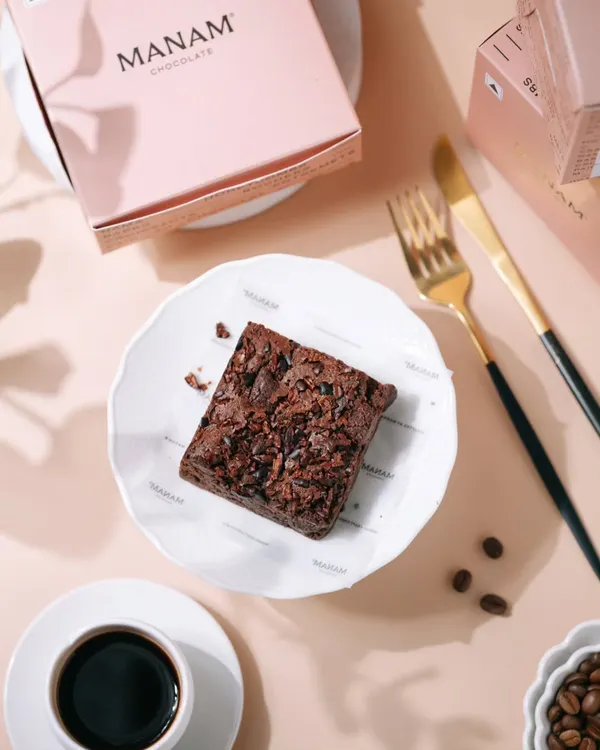 A top-down shot of a rich chocolate brownie from Manam Chocolate, paired with black coffee. This clean, bright styling is perfect for social media and menu photography.