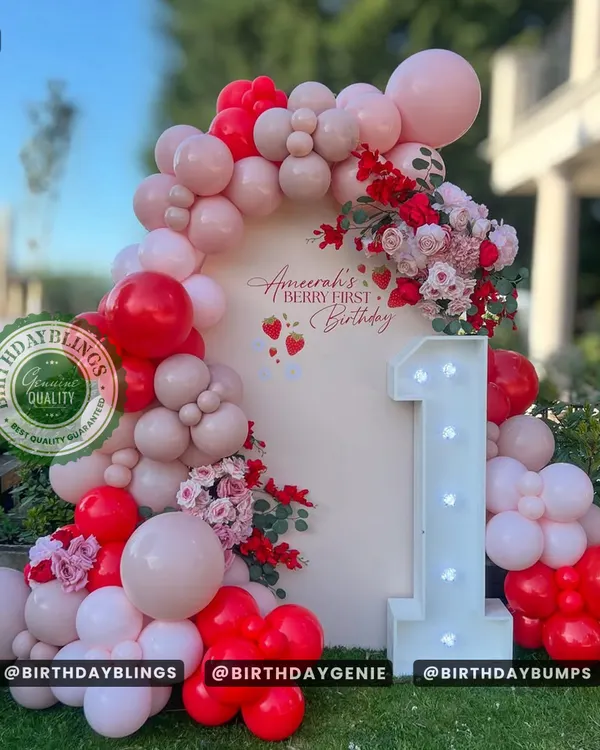 A "Berry First Birthday" theme is a sweet way to celebrate turning one. This outdoor setup features a beautiful balloon arch in shades of red and pink, with a large light-up number '1'.