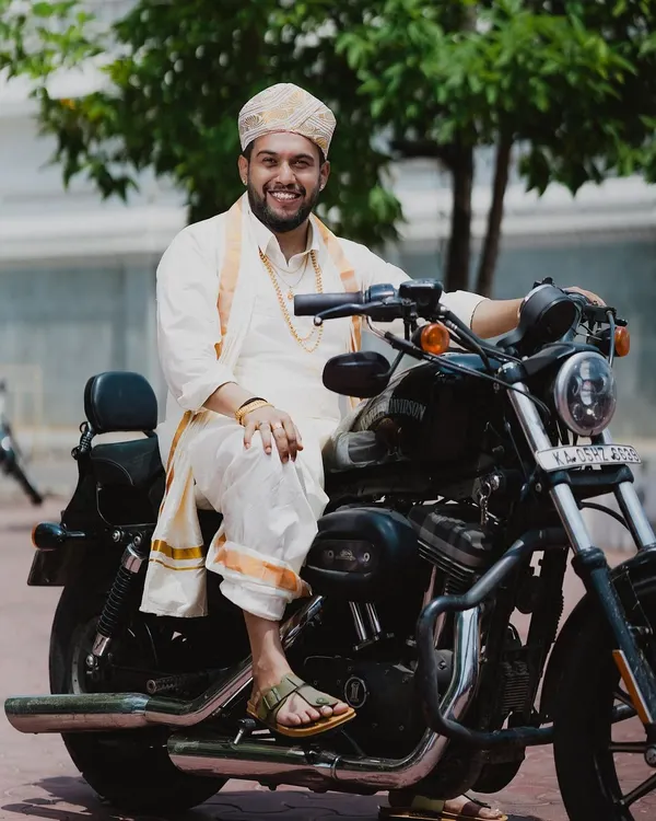 The groom, looking dapper in his traditional attire, poses with a Harley Davidson, blending tradition with a cool, modern edge.