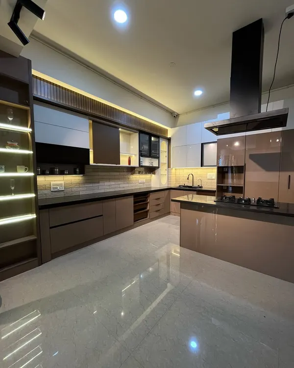 This island kitchen features a beautiful dual-tone acrylic finish. The design includes a built-in hob on the island and a tall unit with illuminated glass shelves, combining functionality with a high-end aesthetic.