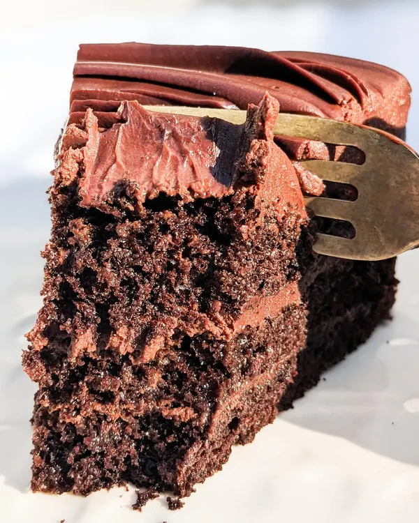 This is what real chocolate cake looks like. A fork sinking into the moist crumb and velvety ganache of our Belgian Dark Chocolate cake, made with real cocoa beans.