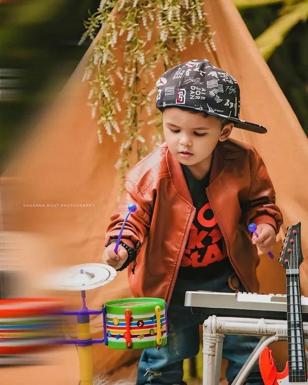 This little rockstar is ready for his concert. With a toy drum set, keyboard, and a cool leather jacket, this themed toddler photoshoot captures a fun and energetic performance.