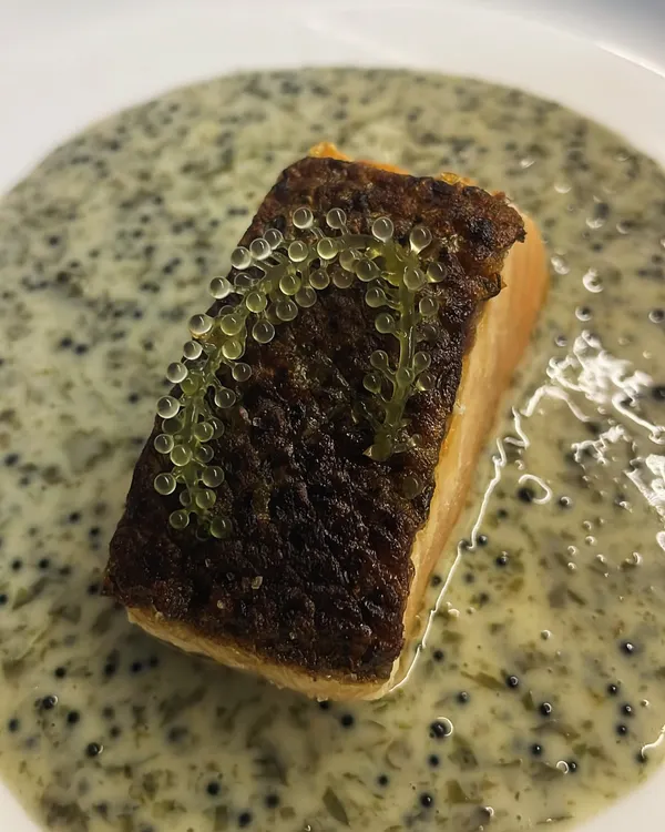 A perfectly seared salmon fillet with crispy skin, served on a creamy sauce with tobiko and garnished with delicate sea grapes for a pop of texture.