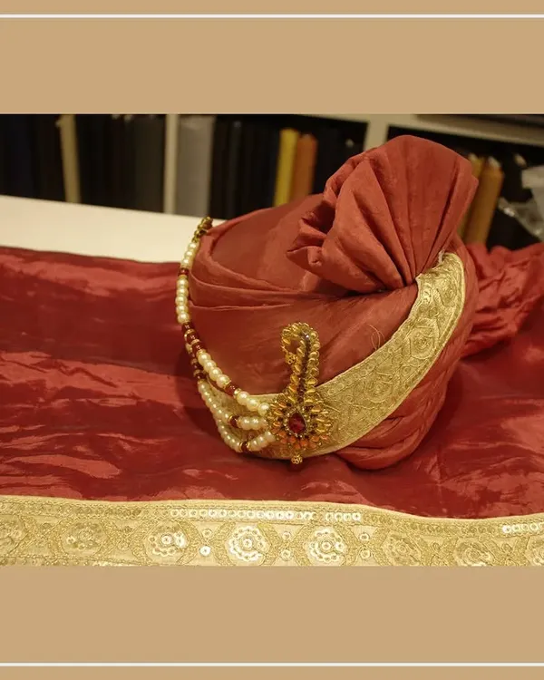A beautiful red groom's pagri (turban) with a gold border and a traditional sarpech (turban ornament). This is a key accessory for a royal wedding look.
