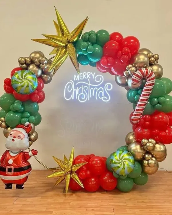 This Christmas-themed balloon wreath is a popular choice for both home and office parties. It combines traditional red and green with metallic gold balloons, a neon sign, and fun accents like a Santa figure and candy cane balloons.