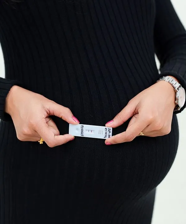 The beginning of it all. A close-up shot of a positive pregnancy test held against the baby bump, beautifully symbolizing the start of a new life and a new journey.