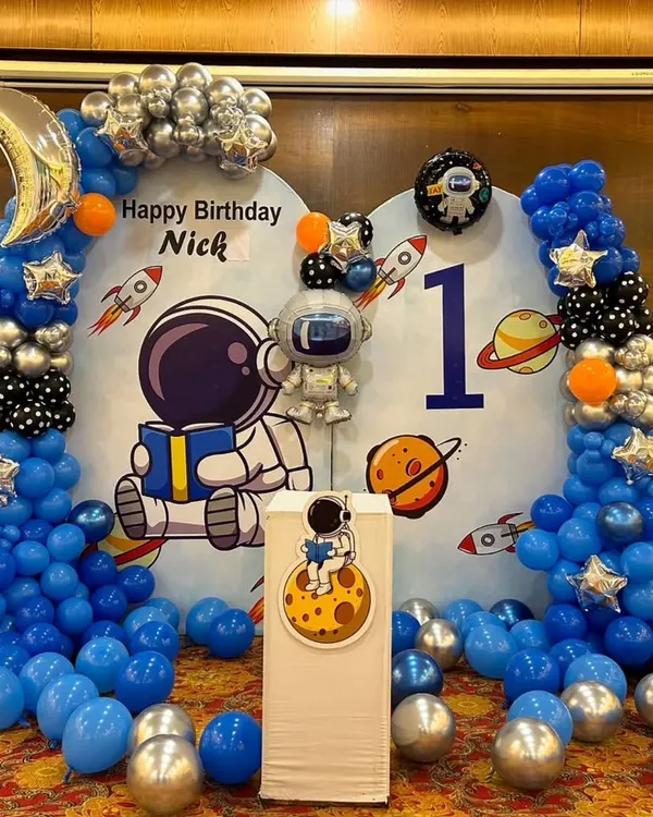 We created an out-of-this-world astronaut theme for Nick's first birthday. The decor includes a custom space backdrop, balloon columns in blue, silver, and black, and special foil balloons like a crescent moon and an astronaut.