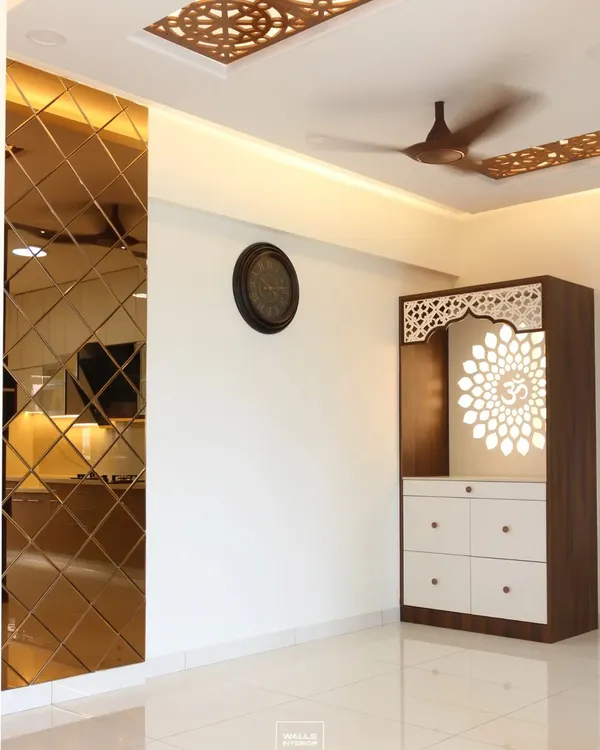 A beautiful free-standing pooja unit with a backlit 'Om' mandala cut into a jali panel. The design is framed by a bronze mirror accent wall and intricate CNC work on the ceiling.