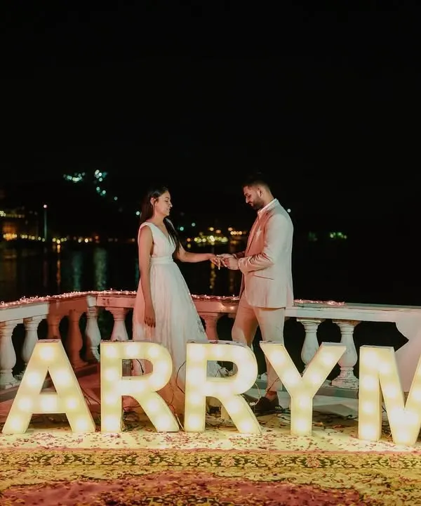 The perfect setup for the most important question. I designed this romantic lakeside proposal with large 'MARRY ME' marquee letters, creating a magical and unforgettable moment against the glittering city lights.