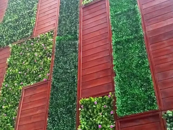 This is a close-up of a large-scale artificial green wall I designed with integrated red-brown wood paneling. The vertical and horizontal lines create a dynamic, modern pattern that completely redefines the building's exterior.