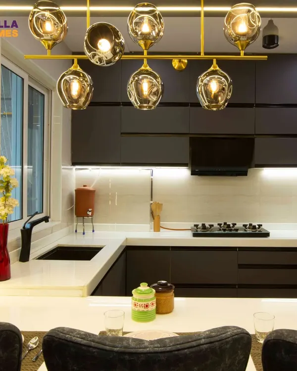 This stunning open kitchen features dark, sleek cabinets, a white countertop, and a beautiful gold chandelier that doubles as a dining light. It's a perfect example of modern luxury.