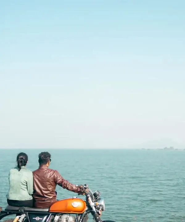Two adventurers looking out at the horizon, seated on their Royal Enfield. This shot captures the promise of the open road and a life of shared journeys by the sea.