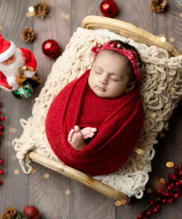 A festive Christmas-themed newborn shoot. A baby swaddled in red on a tiny sleigh, surrounded by ornaments and a miniature Santa, makes for the perfect holiday card.