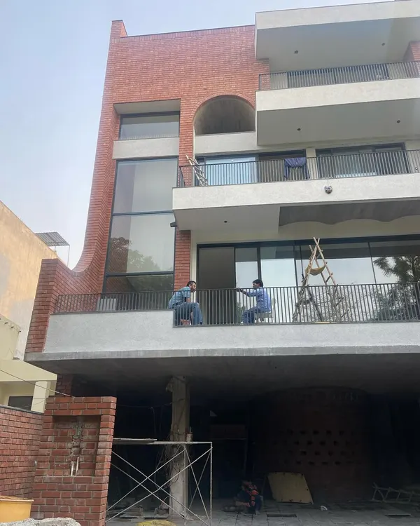 The facade of 'The Waterfall' house in Noida taking shape. This view shows the multi-level balconies and large glass openings that will define the building's exterior, with the sculptural brick element visible at the base.
