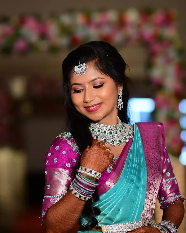 A picture-perfect reception look for Apoorva. The makeup features soft, shimmery eyes and a gentle pink lip, paired with diamond jewellery and a beautiful turquoise and pink saree.