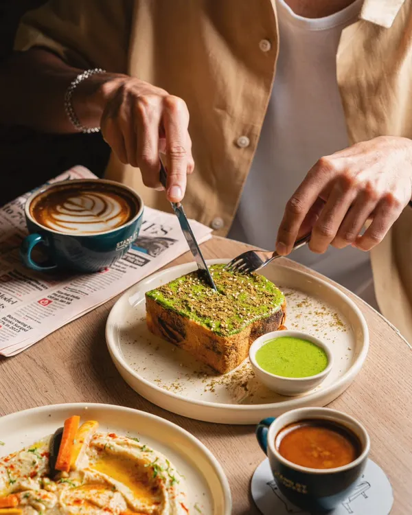 This shot for Stand By Coffee captures food in the context of a meal. The hands cutting into the toast, the latte art in the coffee, and the newspaper on the table create a complete lifestyle scene that feels authentic and inviting.
