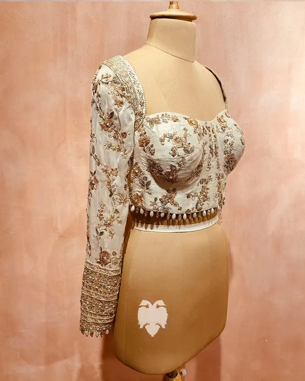 A modern heirloom for Shahin Begum. This corset-style blouse in soft beige raw silk with flowing georgette sleeves is a blend of contemporary charm and traditional finesse.