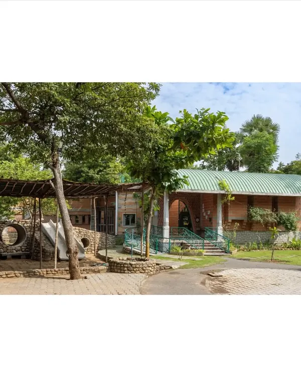 The entrance to the Foothill Learning Centre is designed to be welcoming and integrated with nature. The structure combines rammed earth walls, a green roof, and an open play area, immediately establishing a connection to the outdoors.