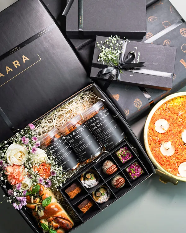 Our Sancho Box is the ultimate Diwali indulgence. It combines a box of our signature sweet bites with savoury jars, a freshly baked bread loaf, and fresh flowers, all presented in our elegant black CAARA box.