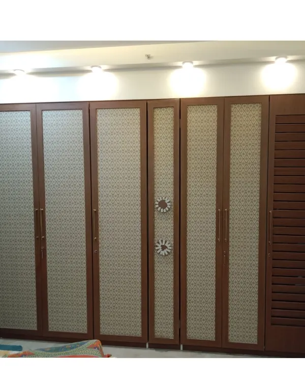 This floor-to-ceiling wardrobe features a unique design with patterned laminate panels and a louvered shutter for ventilation. The custom handles add a decorative touch to the functional storage unit.