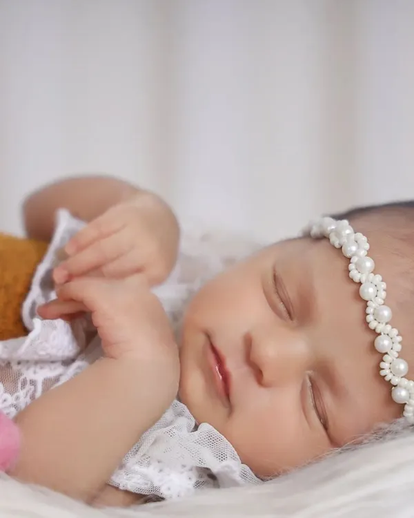 A detailed close-up shot allows us to capture the serene expression of a sleeping newborn. The delicate lace outfit and pearl headband add a touch of elegance without distracting from the baby's natural beauty.